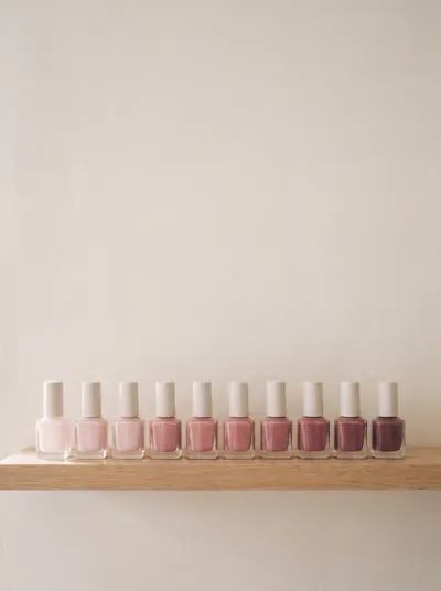 Fileira de esmaltes em tons nude e rosados, sobre prateleira de madeira clara